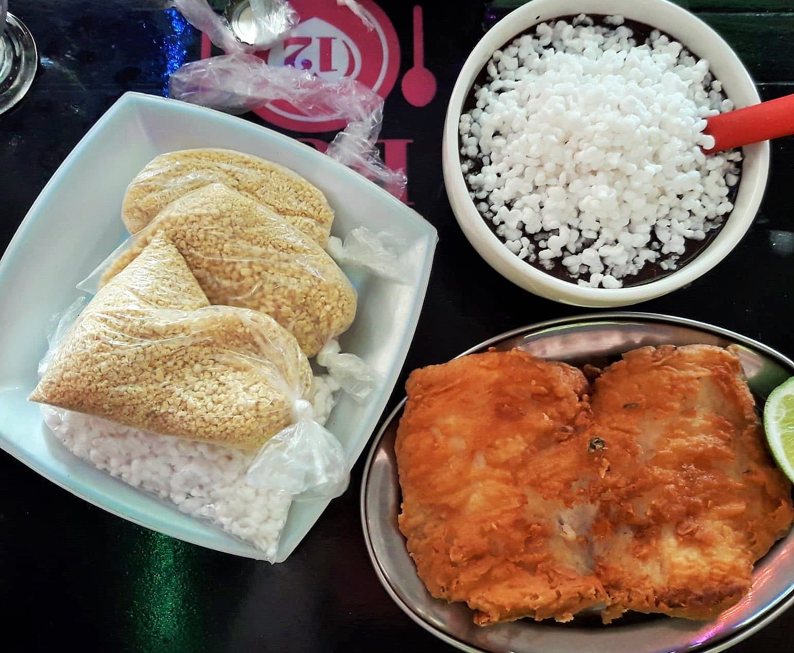 Bowl of unsweetened açaí topped with tapioca pearls, served in Belém, Pará, with bags of farinha and a plate of fried fish alongside