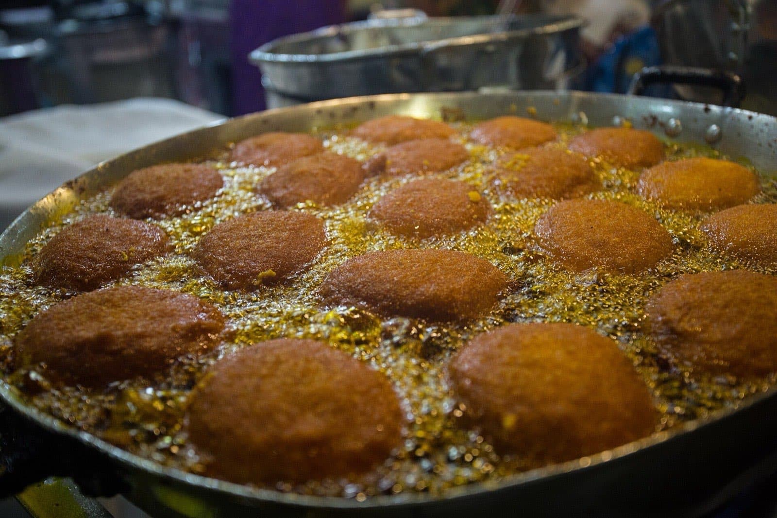 Acarajé fritters frying in a wide pan of bubbling red dendê palm oil at a stall in Salvador, Bahia