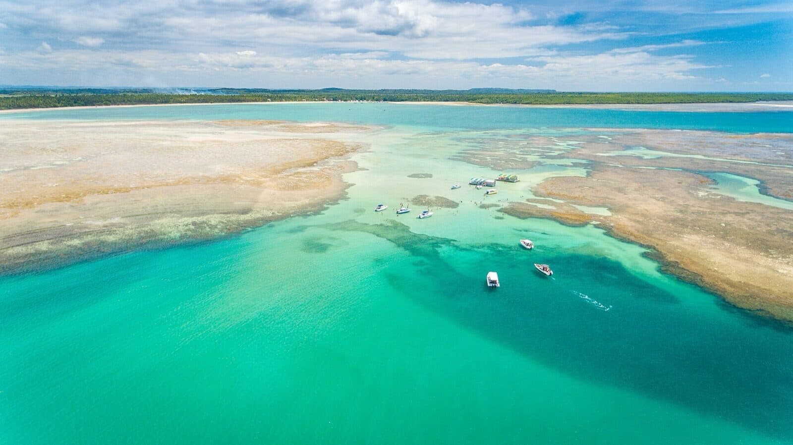 Aerial view of the turquoise natural pools and sandbanks off Garapuá, with Volta à Ilha tour boats moored on the shallow reef flats and swimmers standing in the clear water