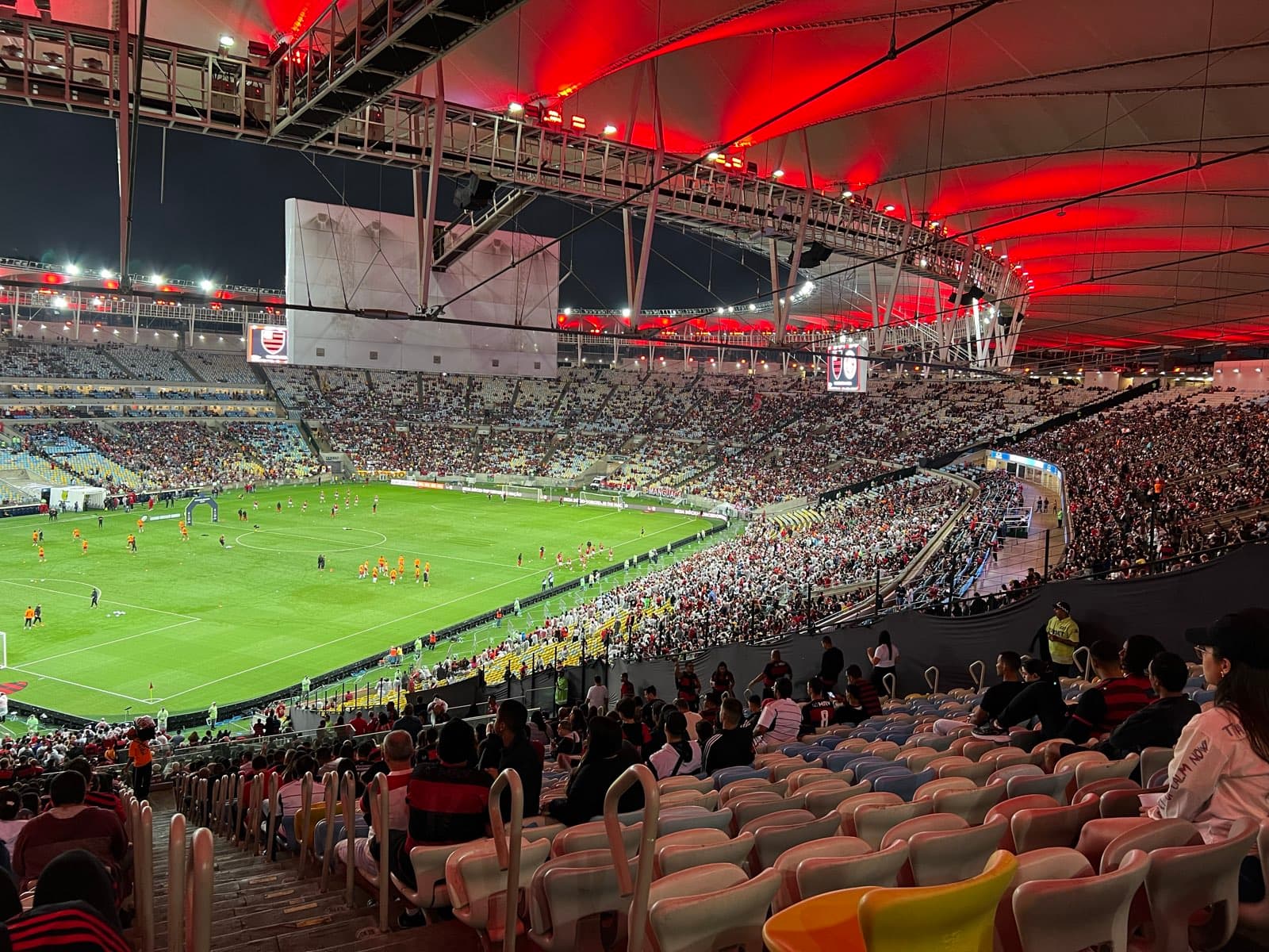 View over the Maracanã pitch from an upper-tier seat before a night Flamengo match, with players warming up and the roof lit in red