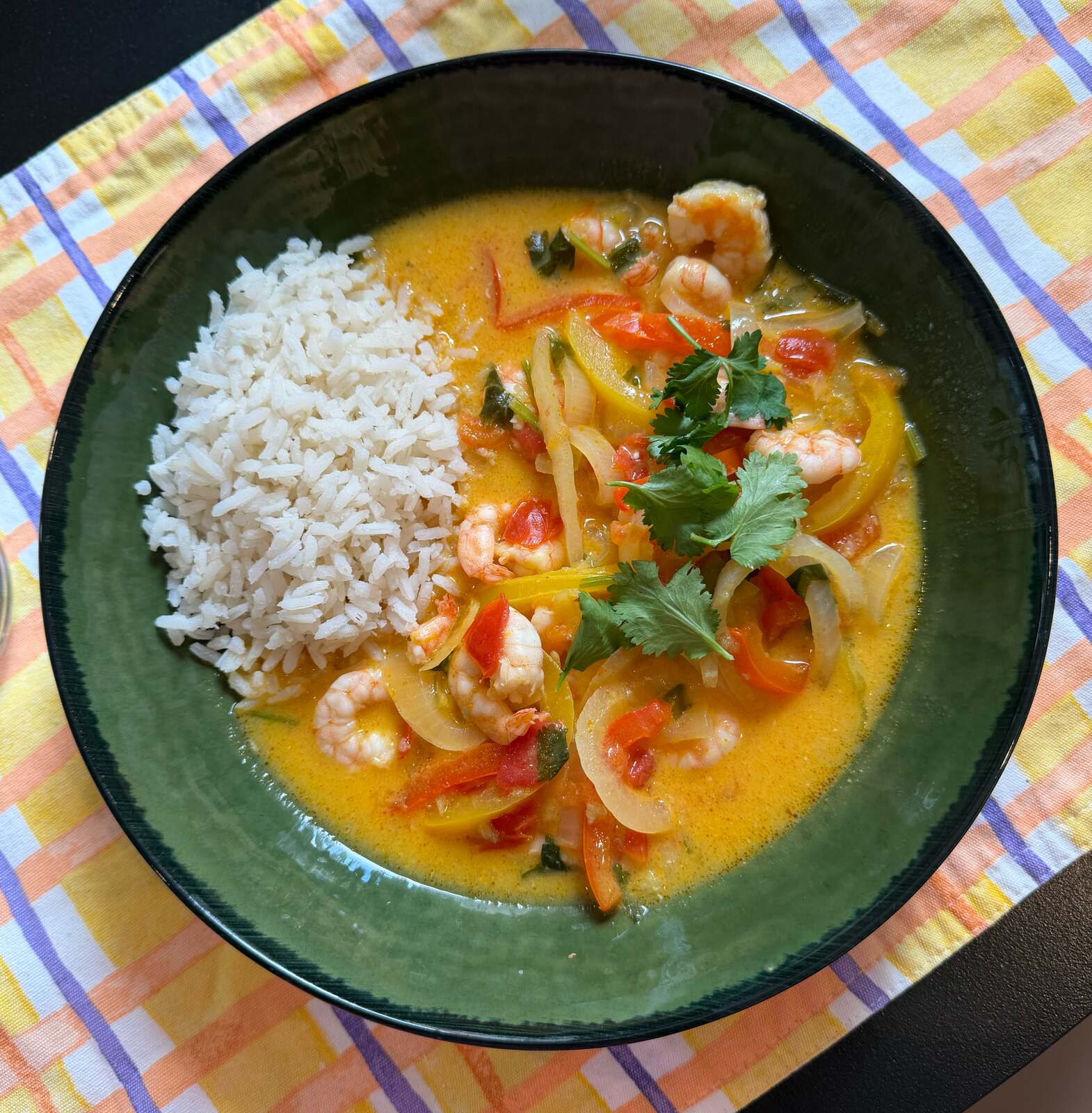 A bowl of shrimp moqueca baiana in a golden coconut broth with sliced onions, red and yellow peppers, and cilantro, served with white rice