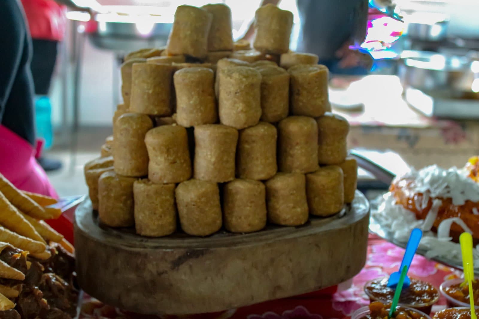 A tower of cork-shaped paçoca, Brazilian peanut candy, stacked on a wooden board on a table with other sweets