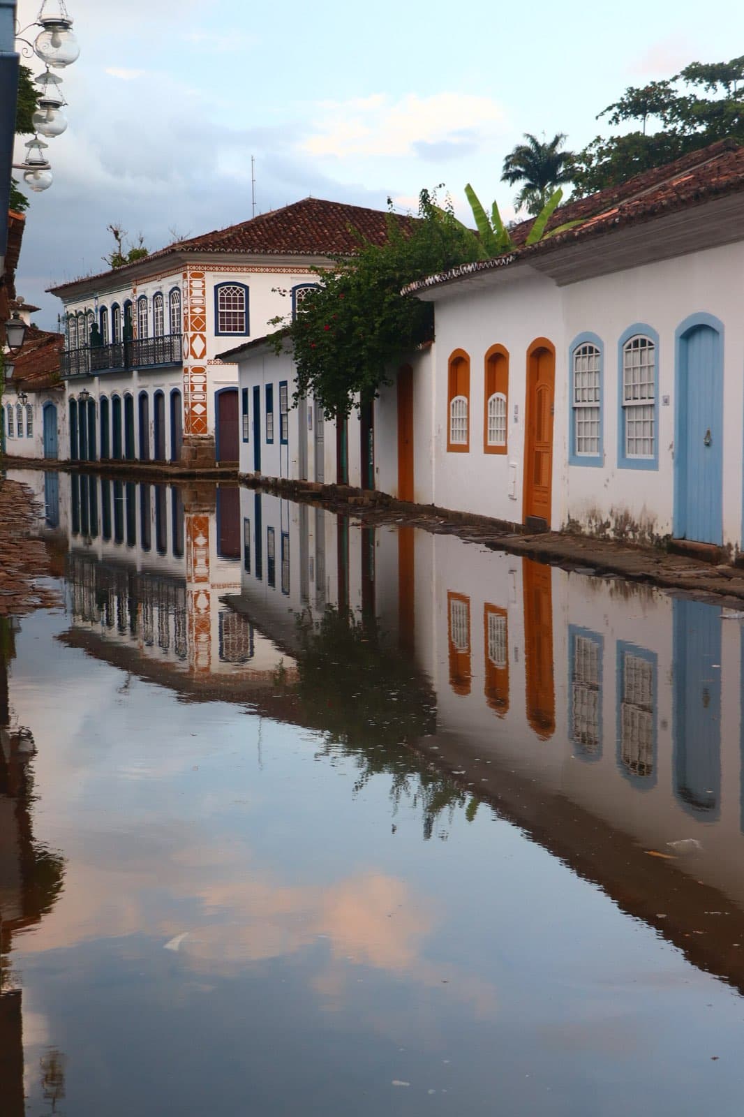 A flooded cobblestone street in Paraty's historic center mirroring whitewashed colonial houses with blue and orange doors and window frames