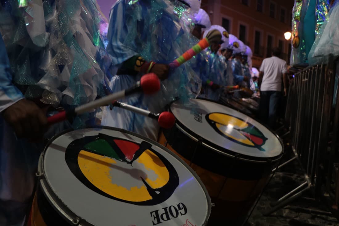 Drummers in shimmering costumes playing large drums at night in the historic center of Salvador during Carnival 2018.
