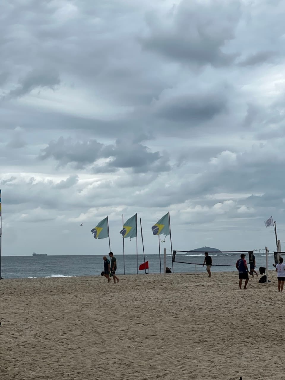 Grey overcast winter sky over Copacabana beach one day later, with Brazilian flags and beach sports nets on the sand