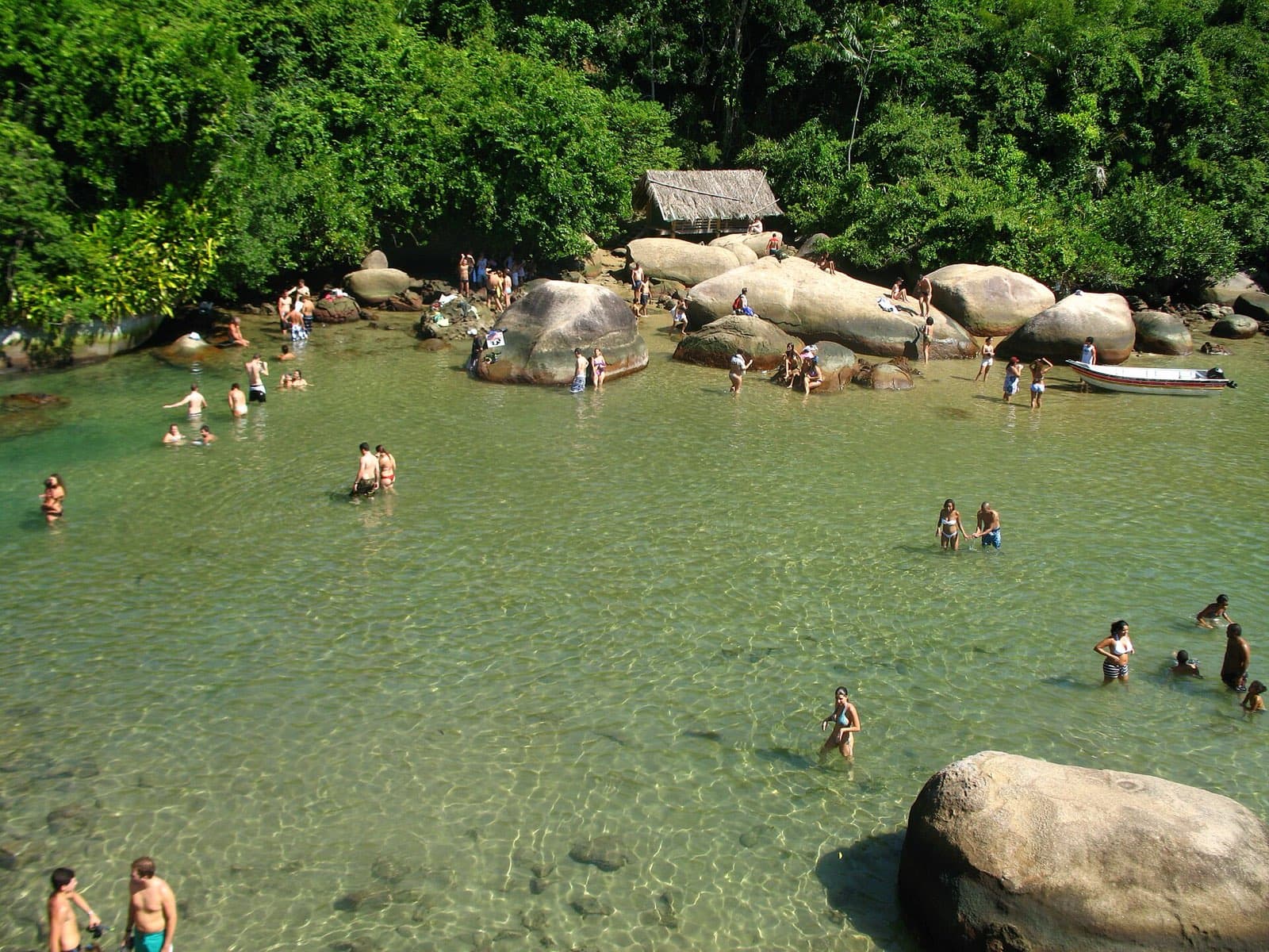 Swimmers wading in the clear, shallow water of the Cachadaço natural pool in Trindade, near Paraty, ringed by boulders and rainforest