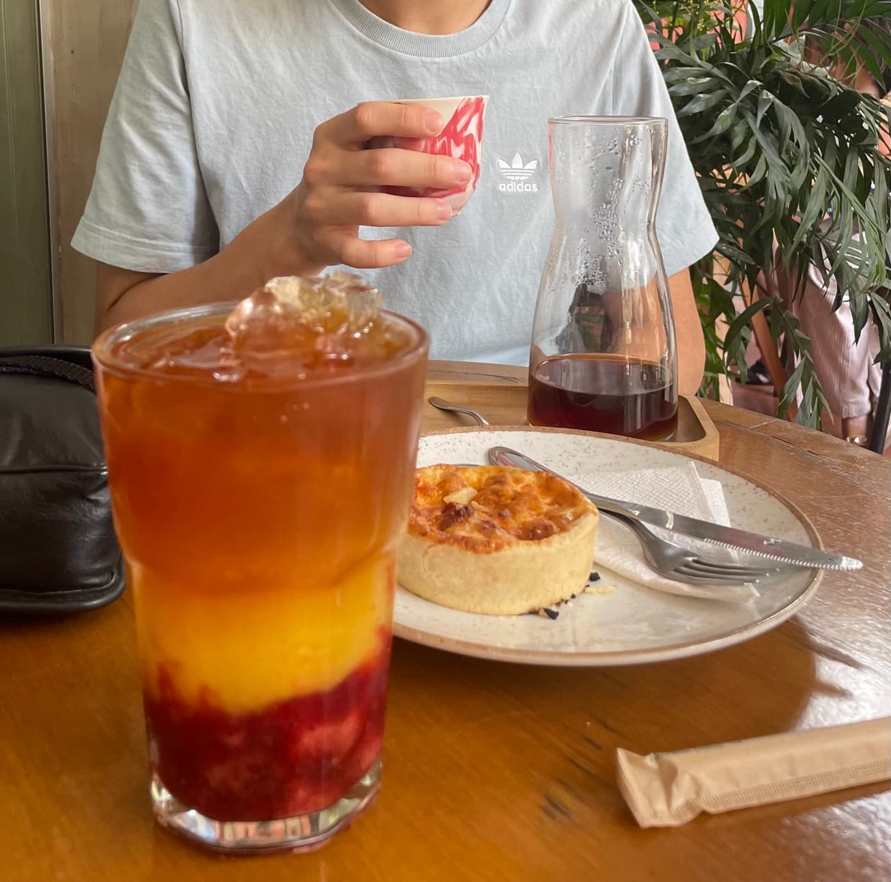 A layered iced fruit drink, a glass carafe of black filter coffee, and a pastry on a wooden table at Academia do Café in Belo Horizonte
