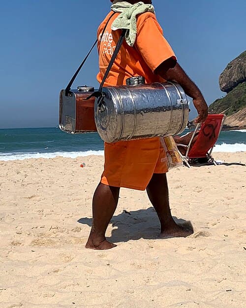 Beach vendor carrying a mate metal cooler on the sand at a beach in Rio de Janeiro