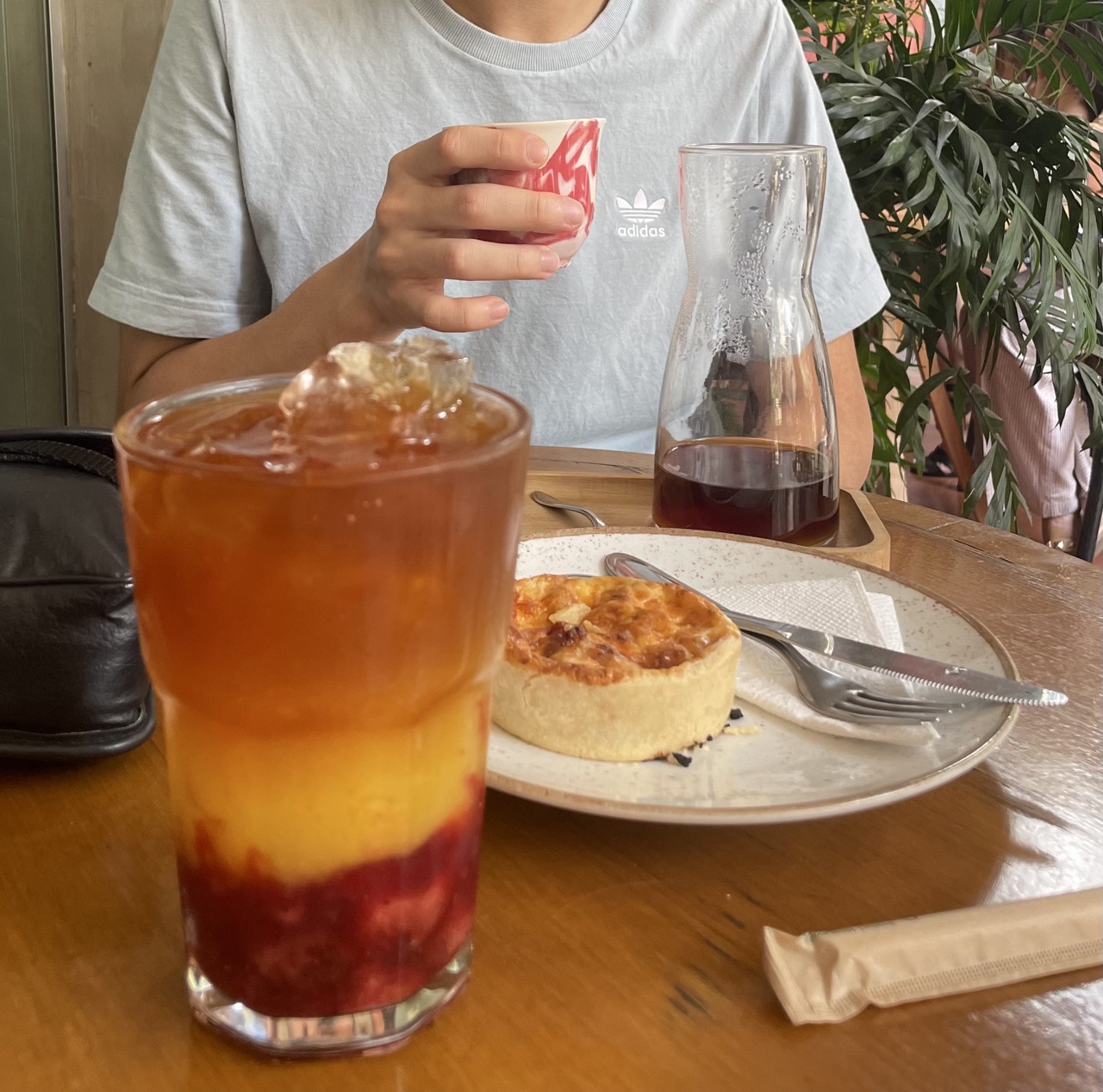 A layered iced fruit drink, a glass carafe of black filter coffee, and a pastry on a wooden table at Academia do Café in Belo Horizonte