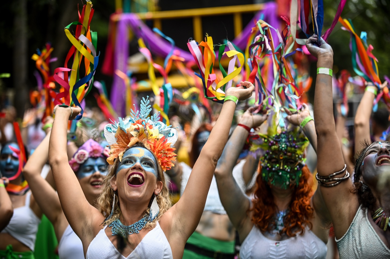Crowd in colorful costumes following the Pena de Pavão de Krishna bloco down a street in the União neighborhood during Carnival in Belo Horizonte.